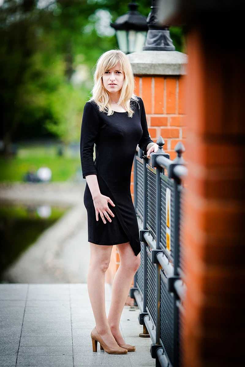 Sesja Modowa Księży Młyn: Modelka w czarnej sukience na tle cegły.